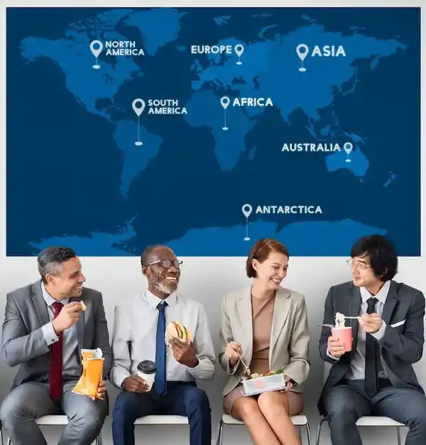 Quatre personnes en tenue professionnelle mangent de la restauration rapide tout en étant assis devant une carte du monde étiquetée avec les continents.