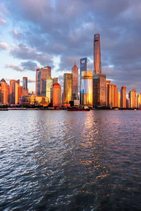 Ville-Shangai Skyline de Shanghai au coucher du soleil avec ses gratte-ciels emblématiques illuminés par la lumière dorée, reflétés dans les eaux calmes du fleuve Huangpu.